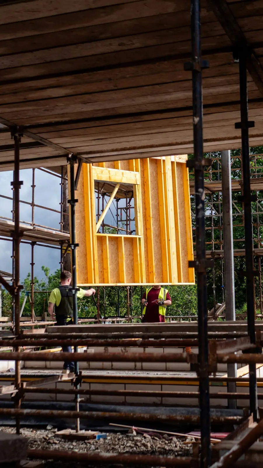 Construction workers lifting a timber wall frame on a scaffolded site