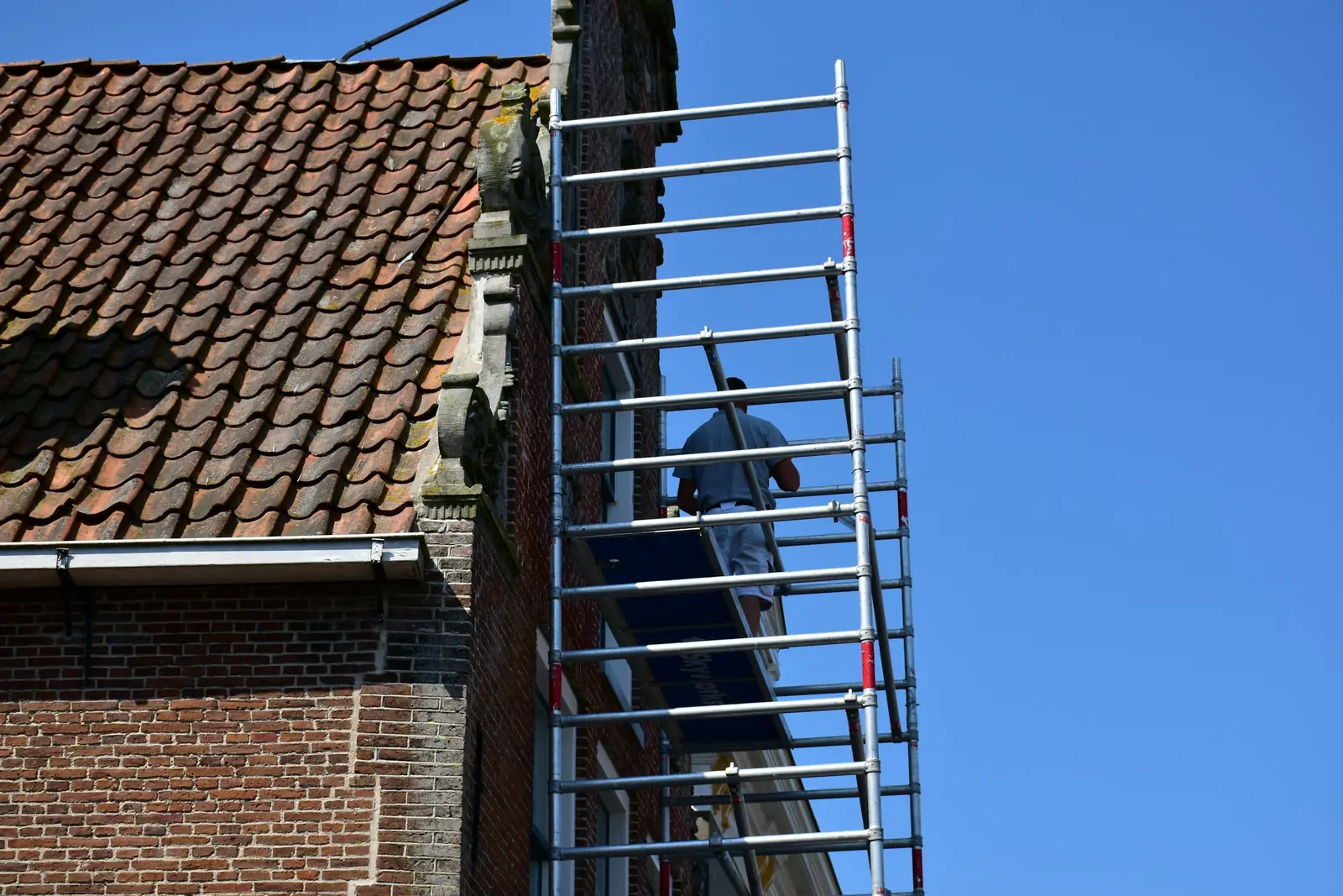 Worker on scaffolding carrying out maintenance on a brick building