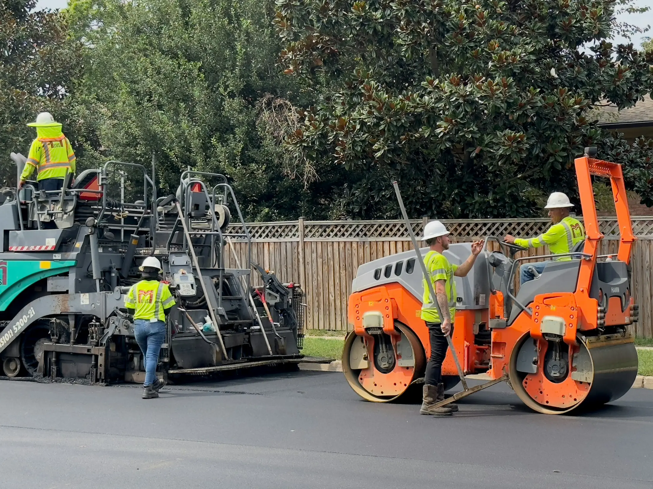 Road crew laying fresh asphalt with a paving machine and roller